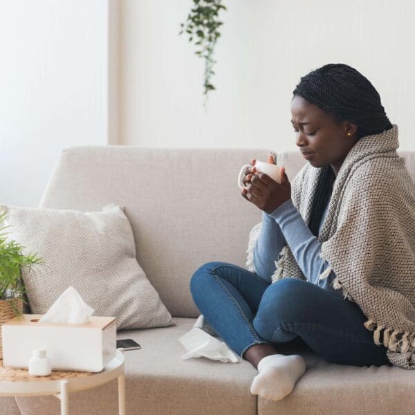 woman sits on sofa holding hot drink scaled