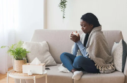 woman sits on sofa holding hot drink scaled