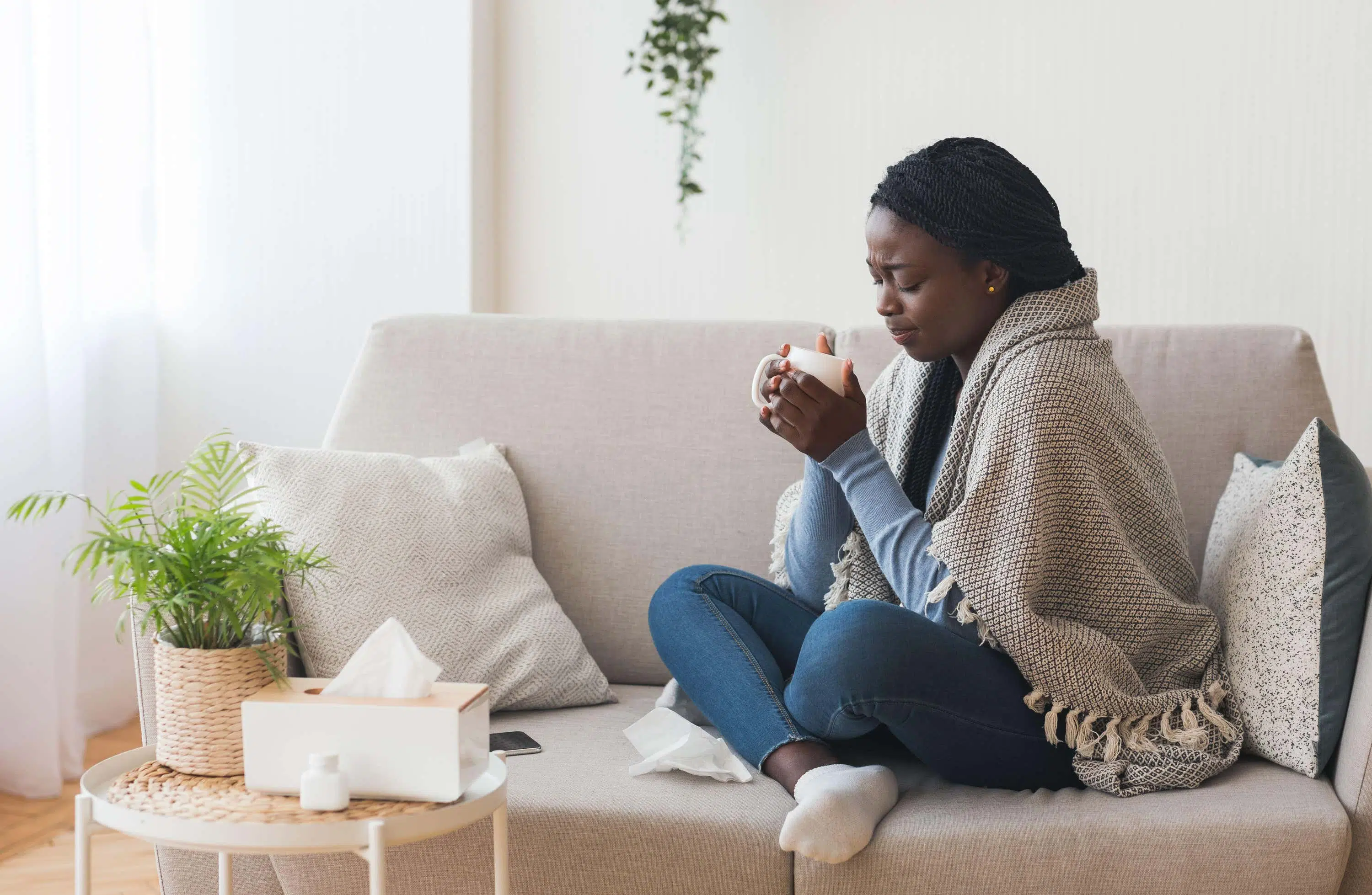Woman sits on sofa holding hot drink scaled