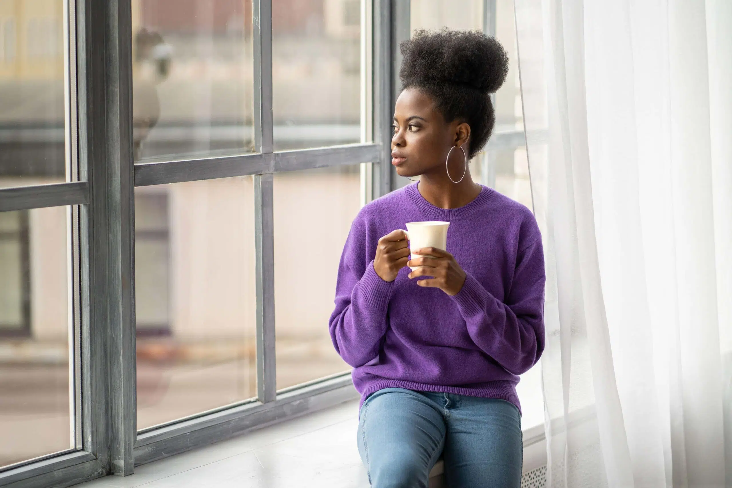 Woman stares out from window with cup in hand scaled