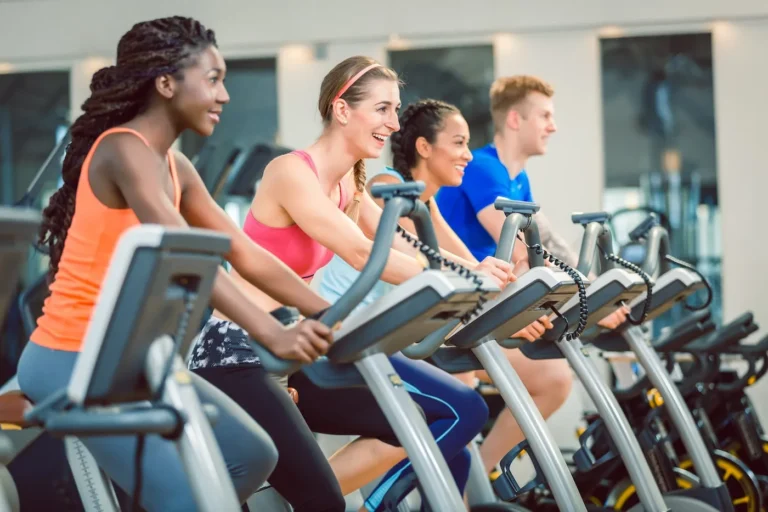 women smiling while cycling on a fitness bicycle during group spinning class at the gym