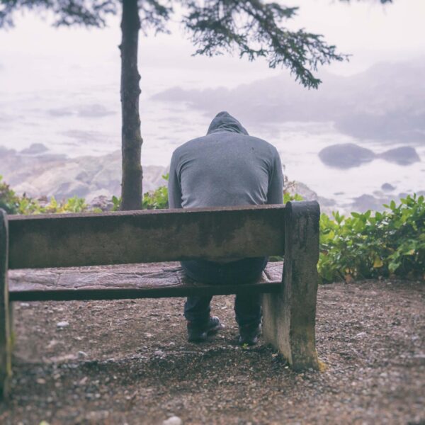 Man looks down while sitting on bench scaled