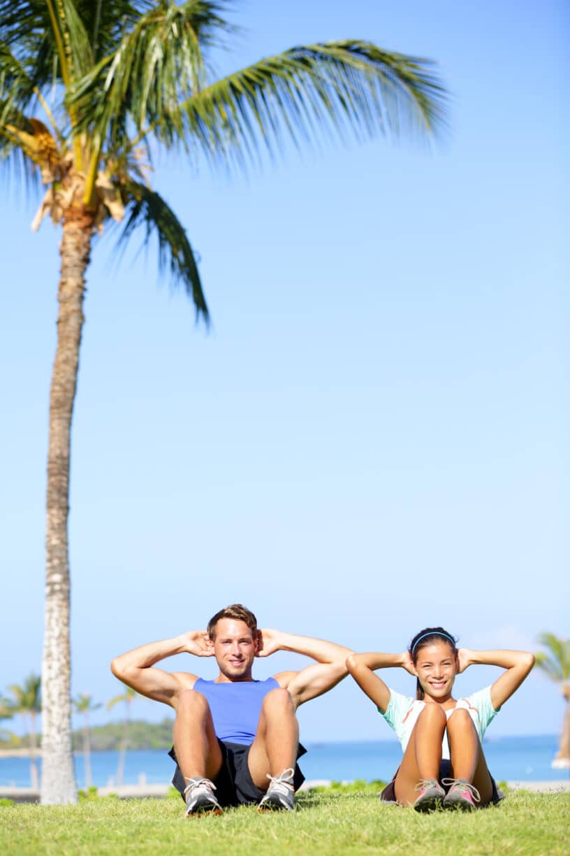 Couple perform situps under palm tree