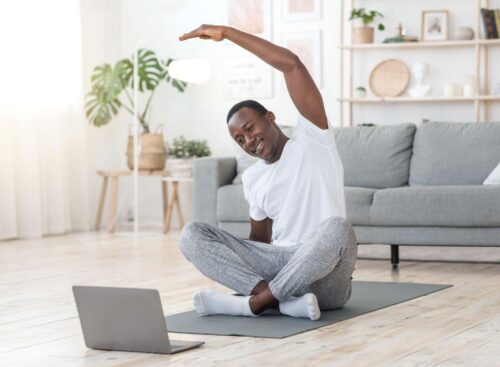 man stretches at home in front of laptop scaled