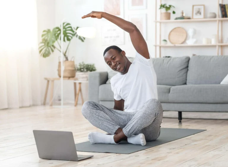 man stretches at home in front of laptop scaled