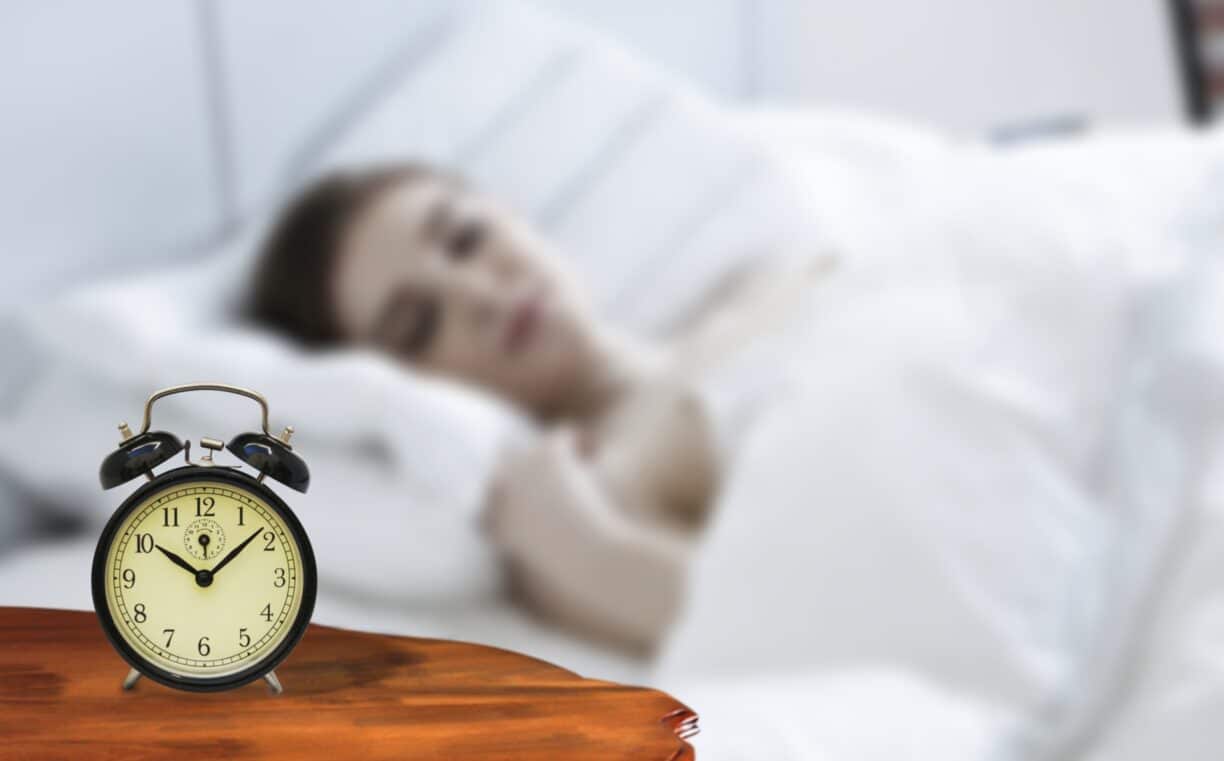 Woman lays in bed looking at alarm clock