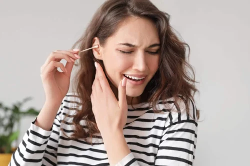 Young woman cleaning ears with cotton bud at home