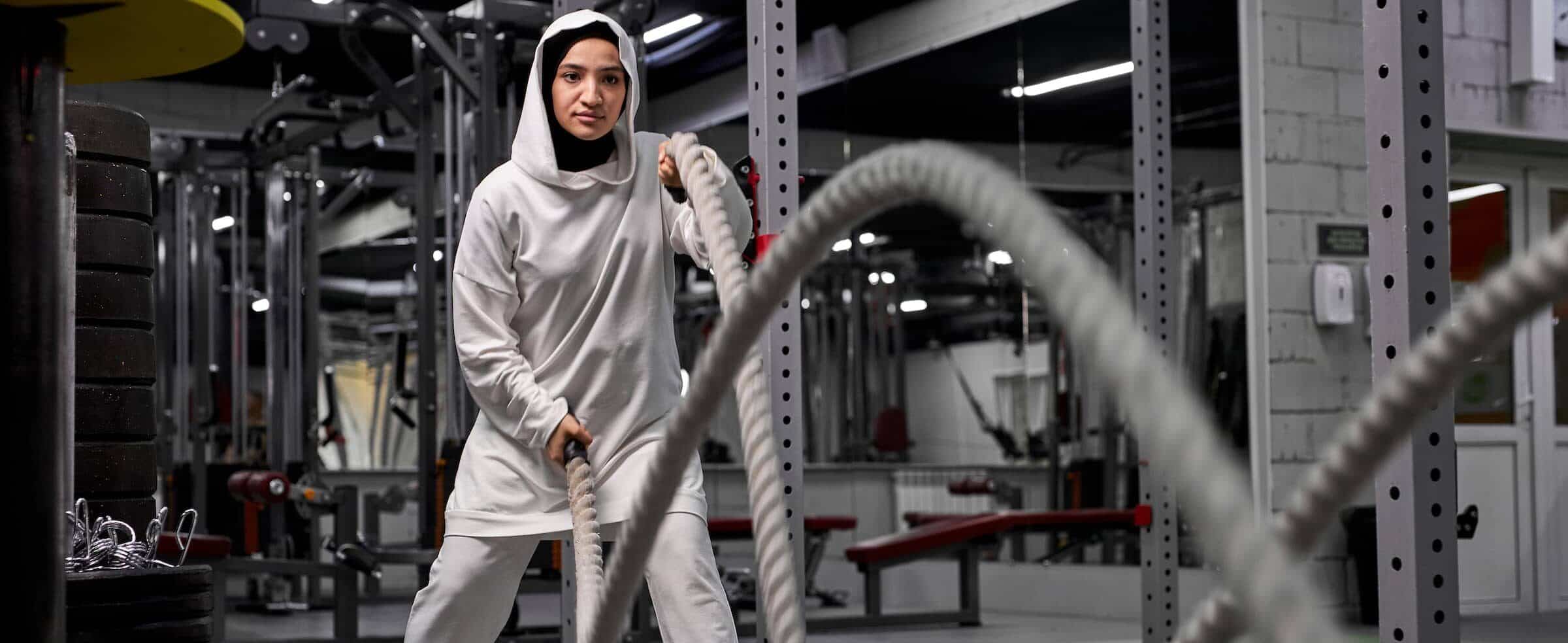 Muslim athletic woman working out with ropes at cross fit gym e1648489953587