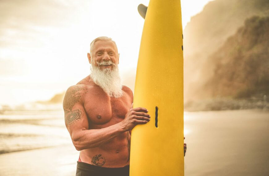 senior surfer holding surf board on the beach at sunset