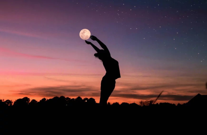 Silhouette of woman bending her back and holding the moon during sunset