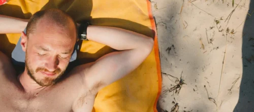 man lays on towel in the sun scaled e1651557472929