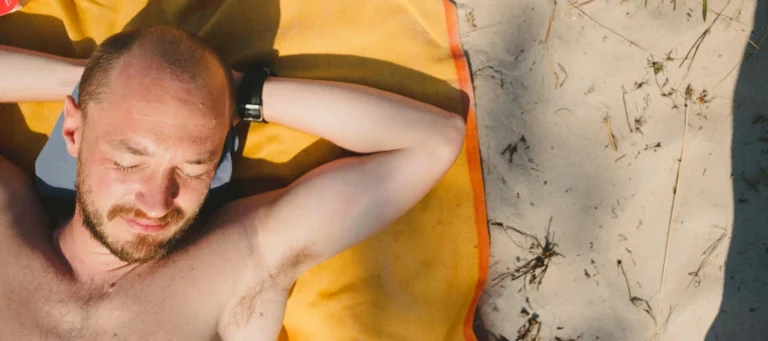 man lays on towel in the sun scaled e1651557472929