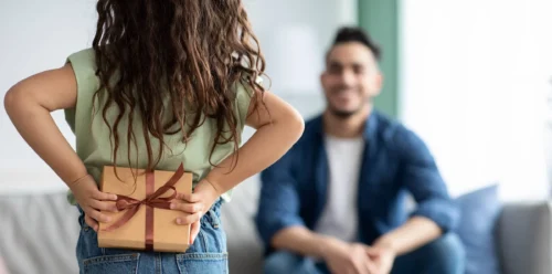 Little girl greeting her dad holding gift behind back