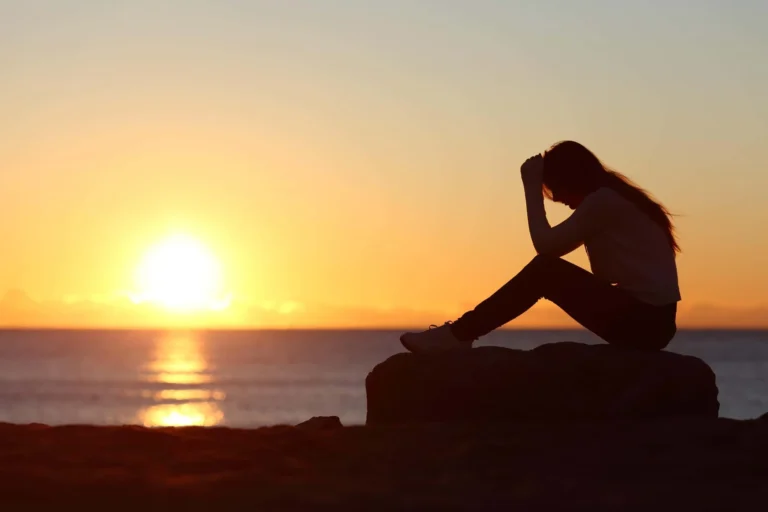 person sits on rock siloutted by the sunset scaled