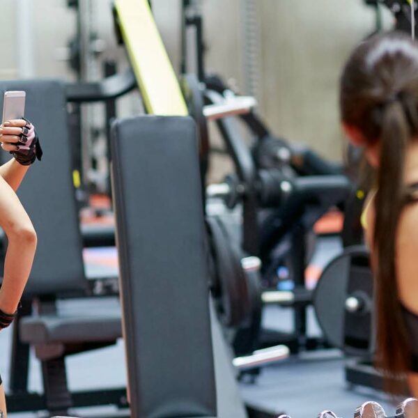 woman with smartphone taking mirror selfie in gym