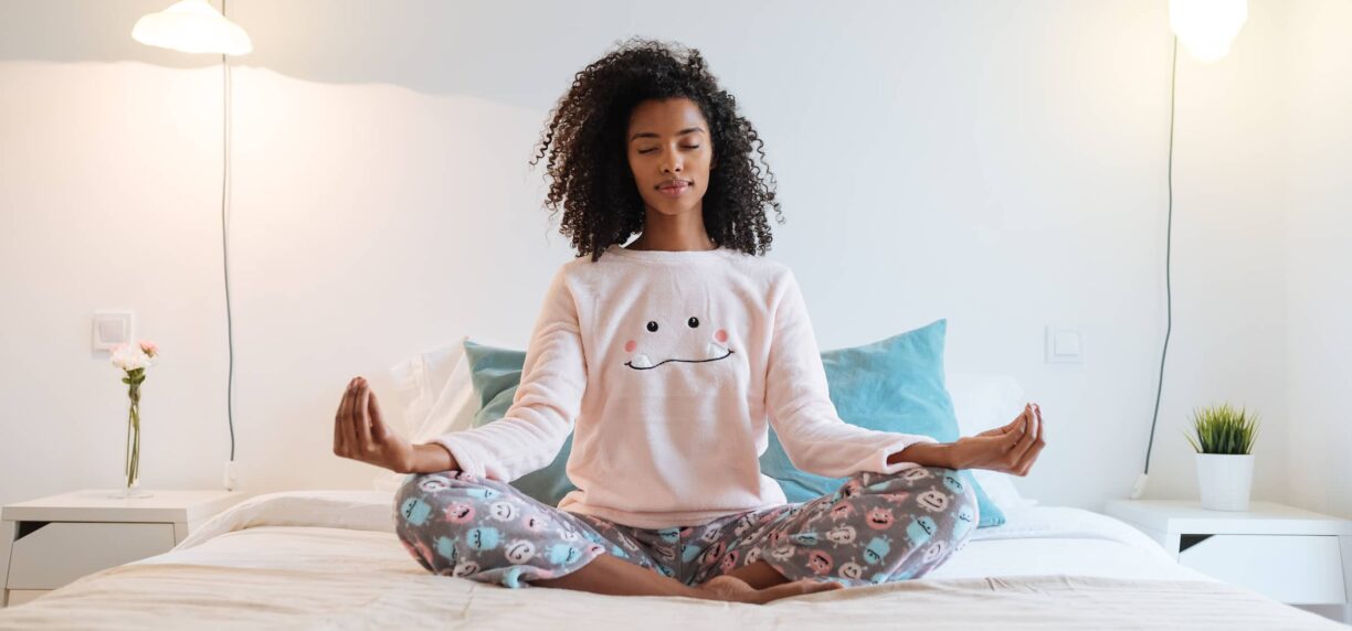 young woman relaxed at home doing morning meditation in bed