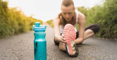 female runner stretching next to bottle of water