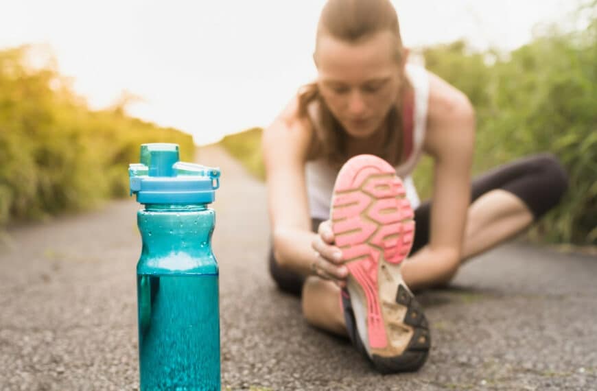 female runner stretching next to bottle of water