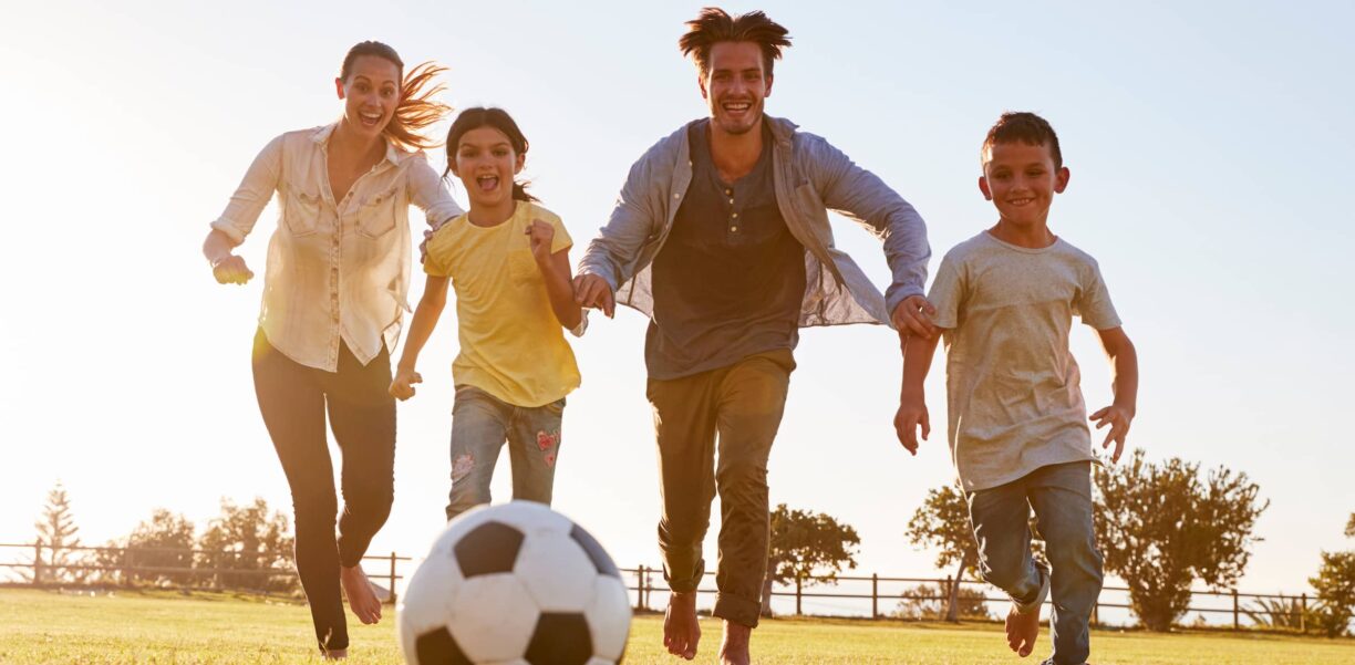 Young family chasing after a football in a park