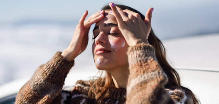 Young woman applying sunscreen on her face in snowy mountains in winter