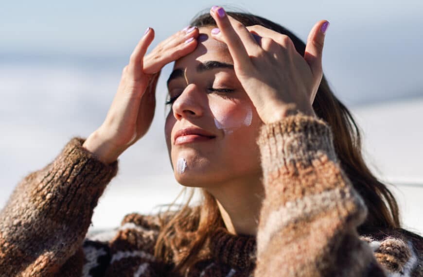 Young woman applying sunscreen on her face in snowy mountains in winter