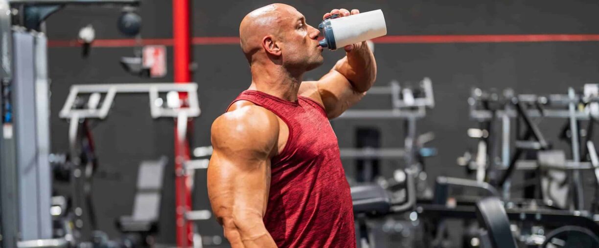 bodybuilder in t-shirt drinking water with protein and supplements for training at the gym