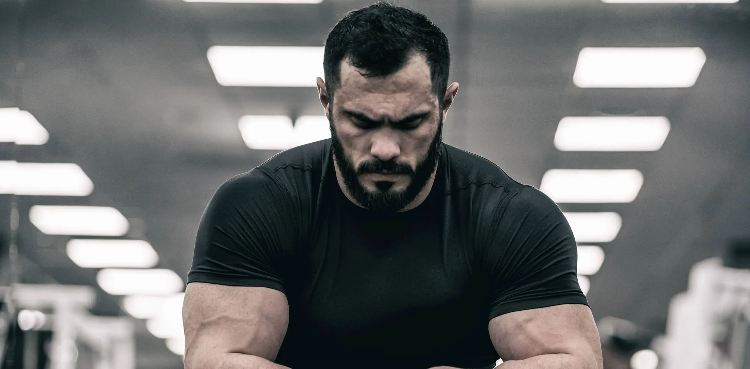 strong man with beard wearing black jersey concentrates in gym