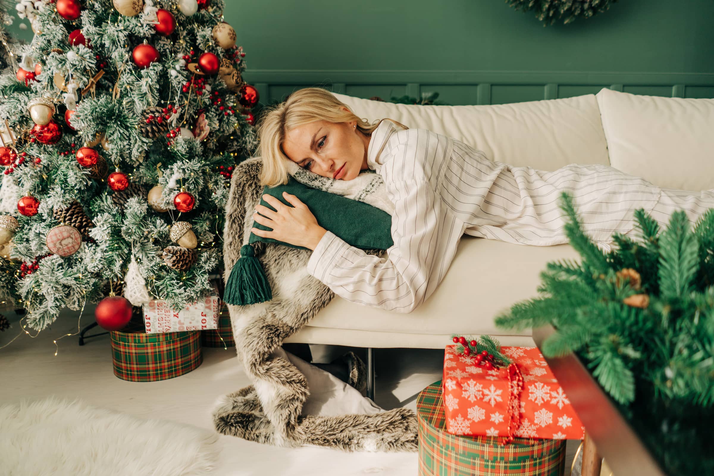 Frustrated sick woman in pyjamas lies on the sofa in christmas alone