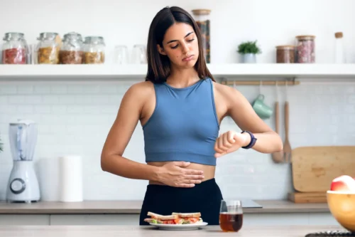 Hungry sporty woman waiting for the time to eat healthy breakfast after fasting in the kitchen at home