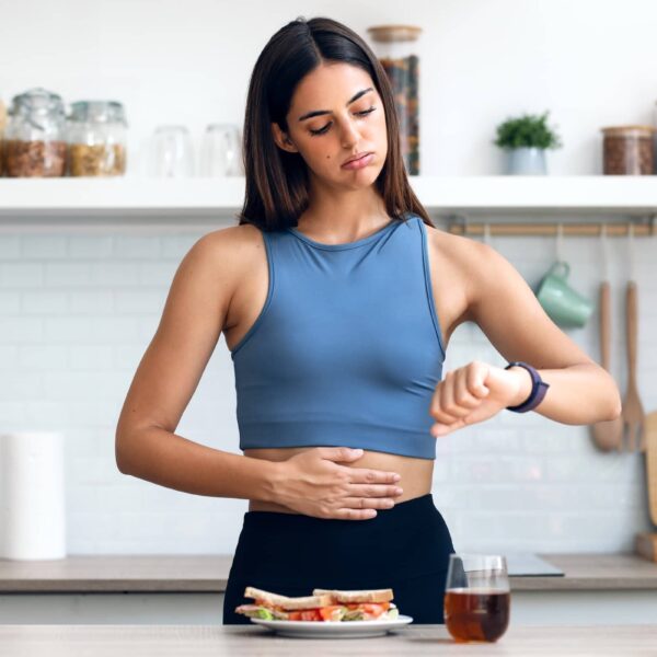 Hungry sporty woman waiting for the time to eat healthy breakfast after fasting in the kitchen at home