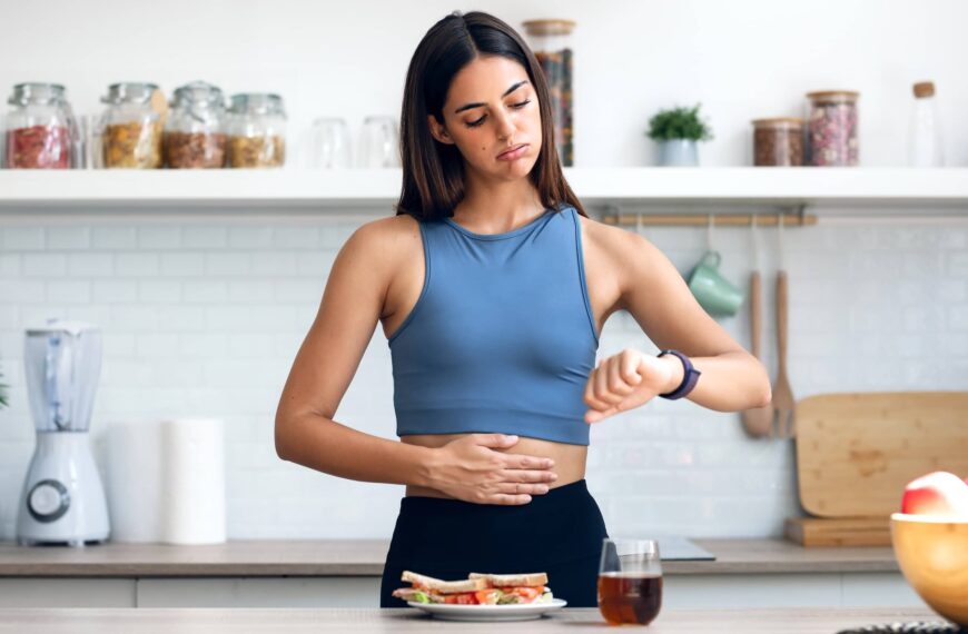 Hungry sporty woman waiting for the time to eat healthy breakfast after fasting in the kitchen at home