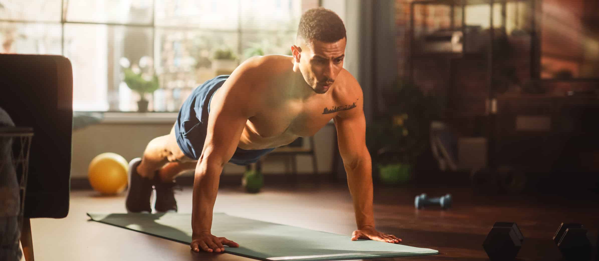 Strong athletic man does shirtless workout at home gym, doing push ups. Lean fit muscular mixed race sportsman staying healthy, training at home. Sweat and determination lead to success
