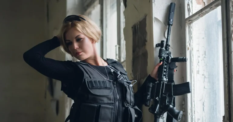 Young woman with airsoft rifle is posing near broken window.