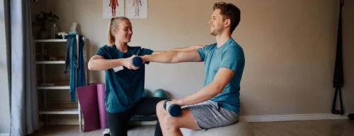 Female nurse helping young man doing stretching exercise in hospital using dumbbells