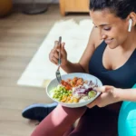 Sporty young woman eating healthy while listening to music sitting on the floor at home