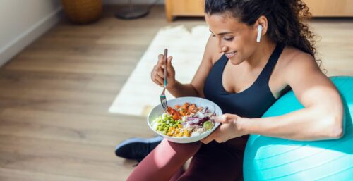 Sporty young woman eating healthy while listening to music sitting on the floor at home