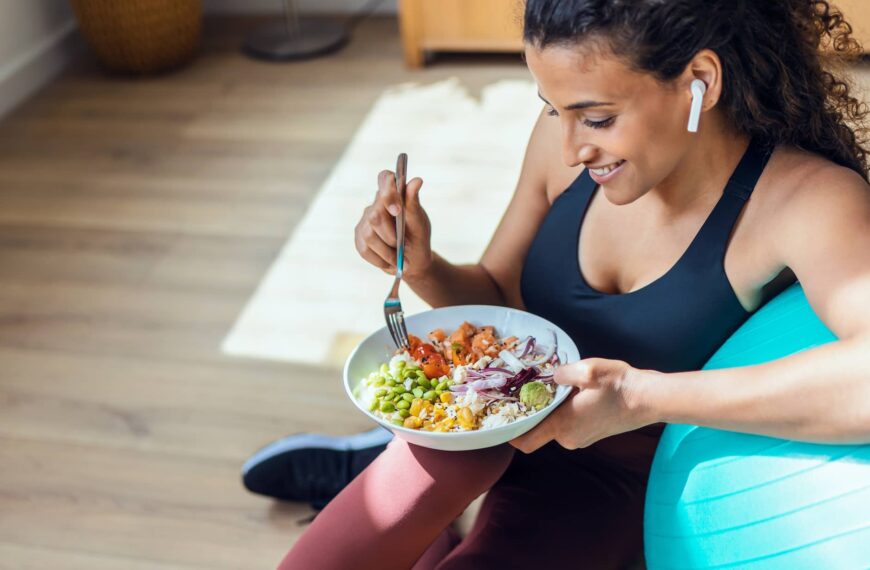 Sporty young woman eating healthy while listening to music sitting on the floor at home