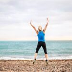 Young sporty woman runner in blue sportswear jumping on the beach outside