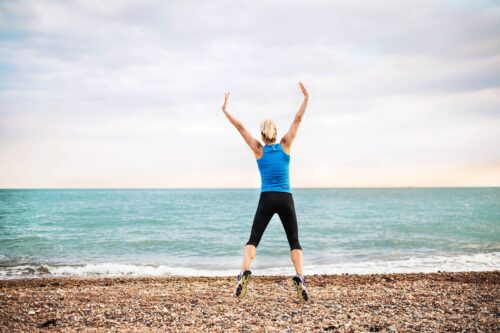 Young sporty woman runner in blue sportswear jumping on the beach outside