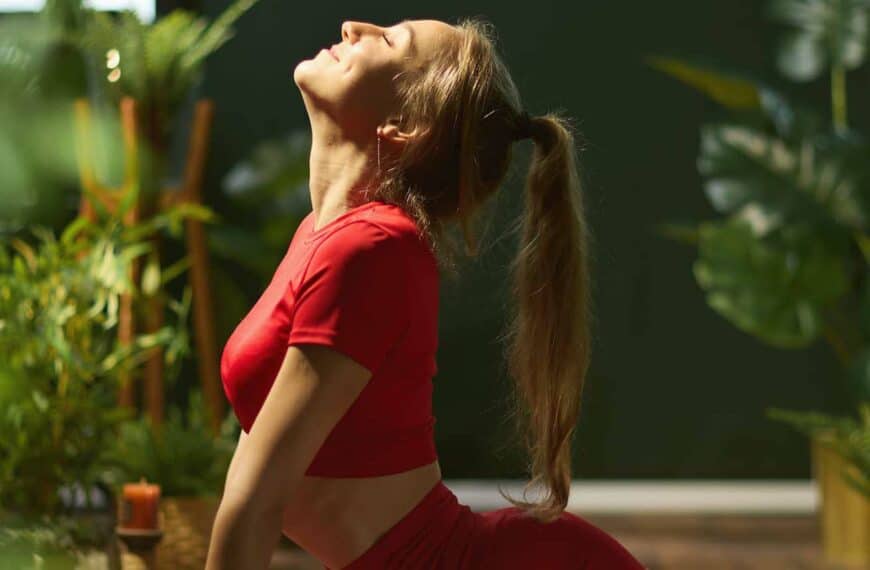 female in red fitness clothes in green living room doing yoga