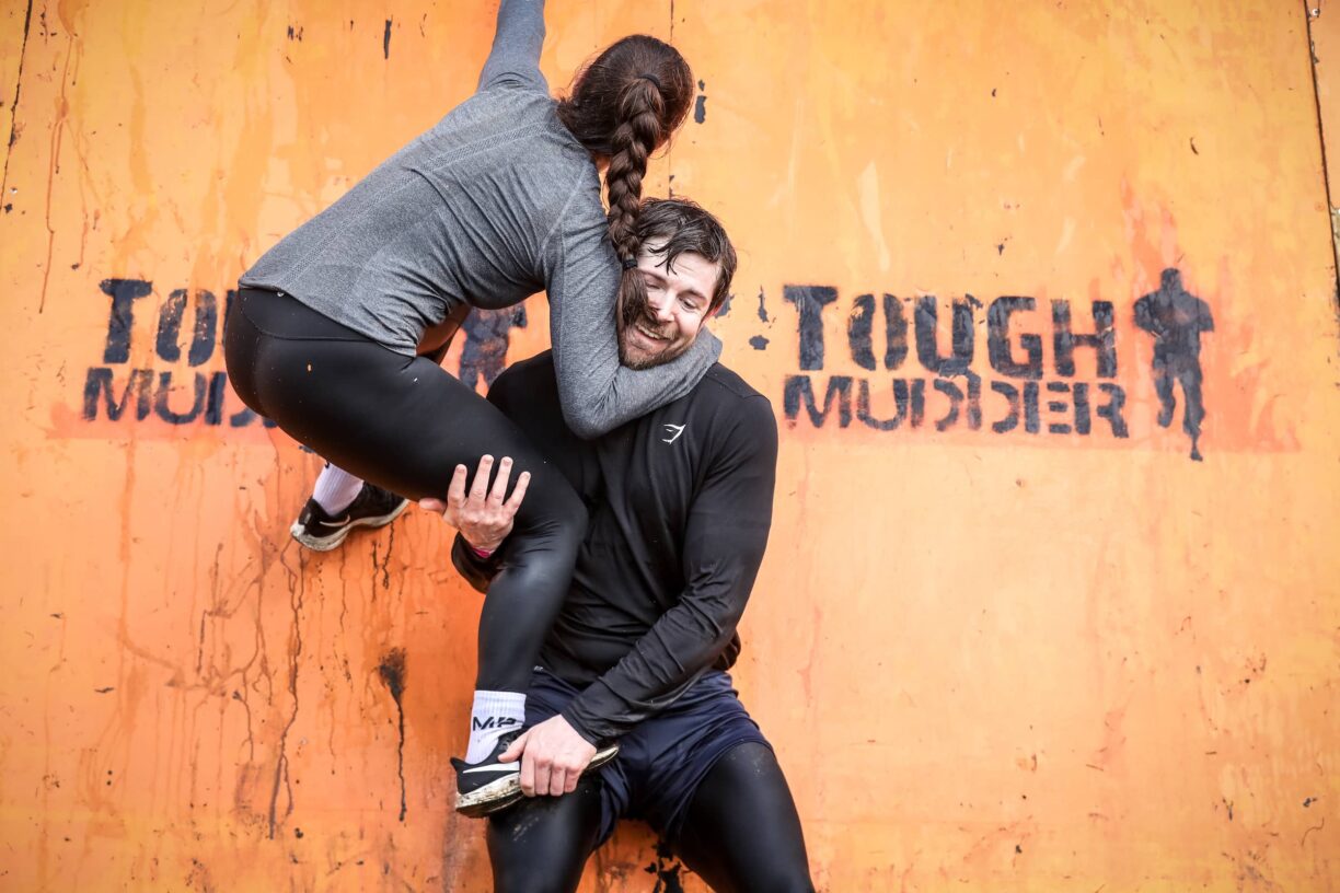 Couple work together to climb wall at tough mudder