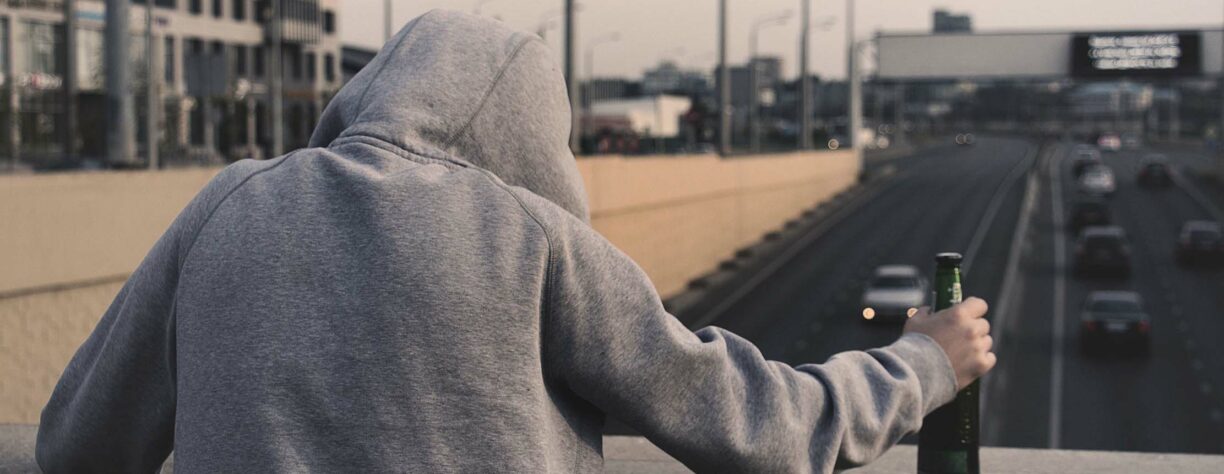 person looks over motorway bridge with alcoholic bottle in hand