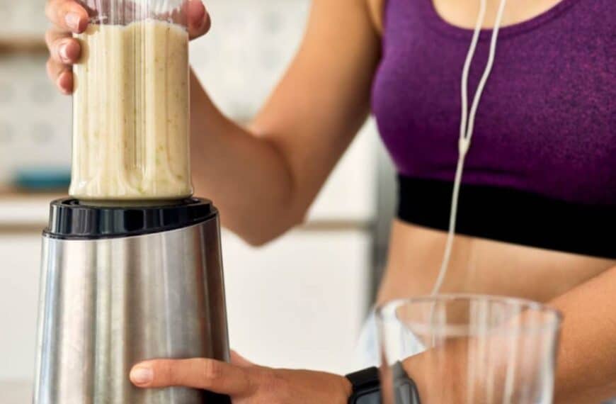 athletic woman using blender and preparing smoothie in the kitchen.