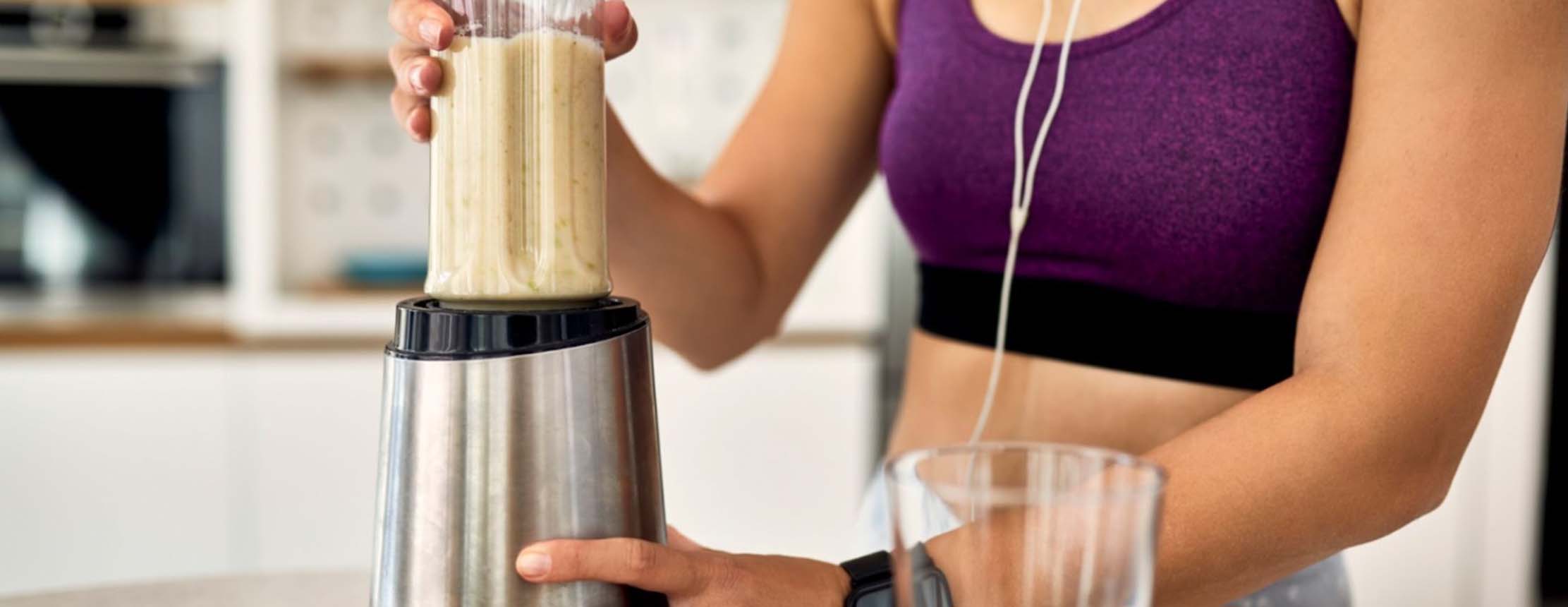 Athletic woman using blender and preparing smoothie in the kitchen.
