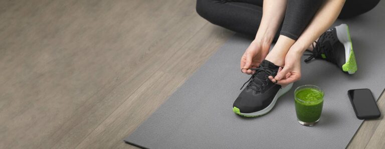 woman ties laces on yoga mat with juice to the side