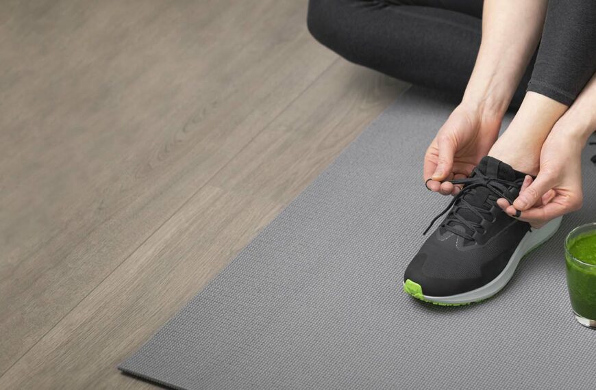 woman ties laces on yoga mat with juice to the side