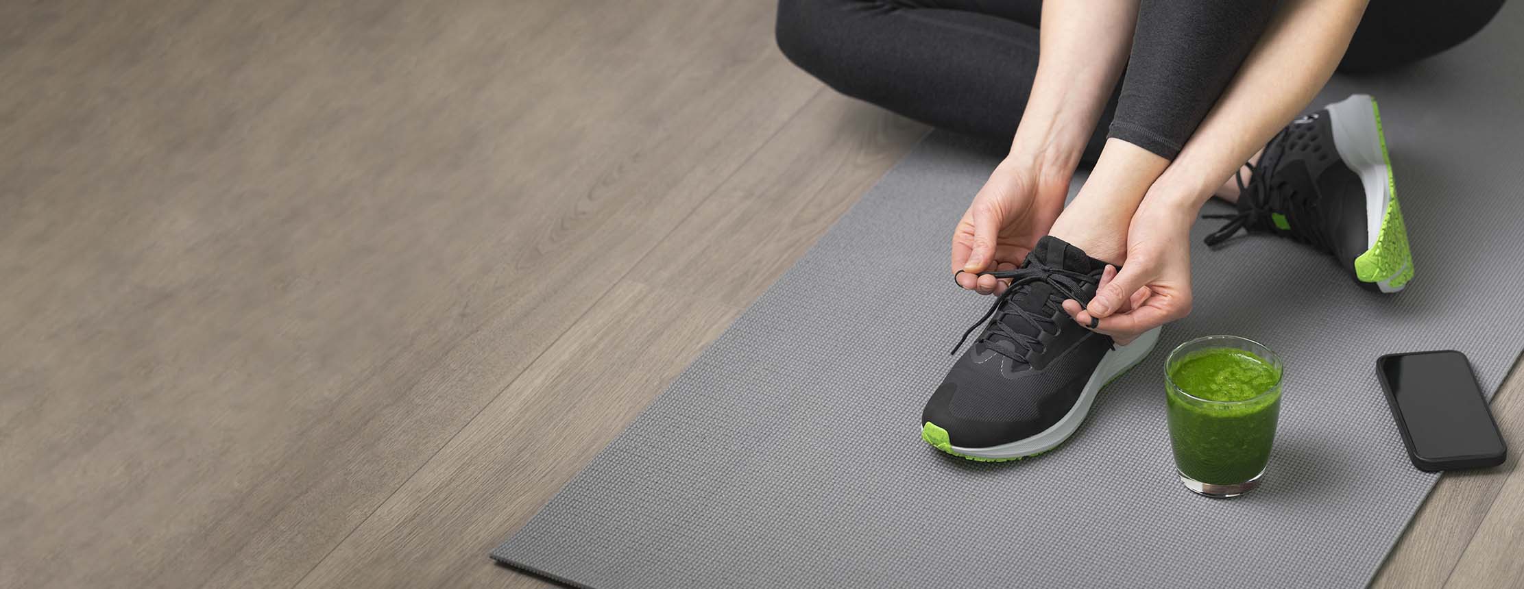 Woman ties laces on yoga mat with juice to the side