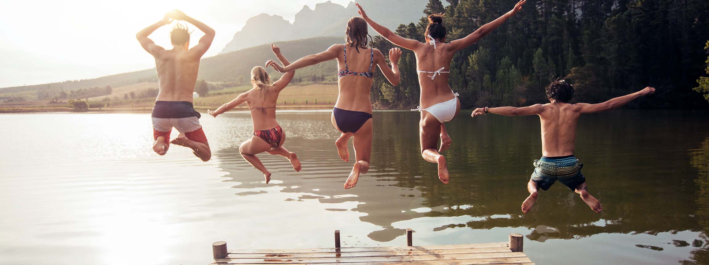 Young friends jumping into lake from a jetty