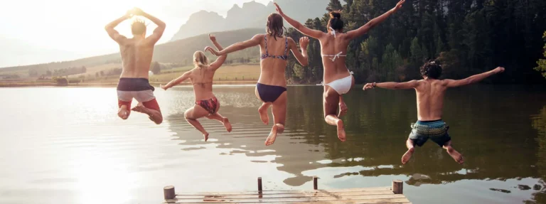 Young friends jumping into lake from a jetty