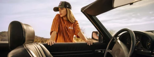 woman leans over car wearing new era trucker cap